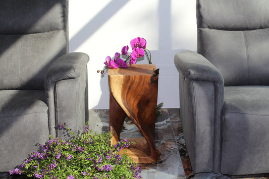 A sculptural solid-wood twist table in warm daylight, between two grey armchairs