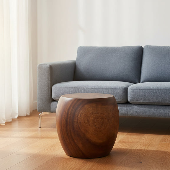 Haussmann MMP pouf stool accent table, 20 in dia x 18 in H walnut oil, in a living room in front of a blue-grey sofa